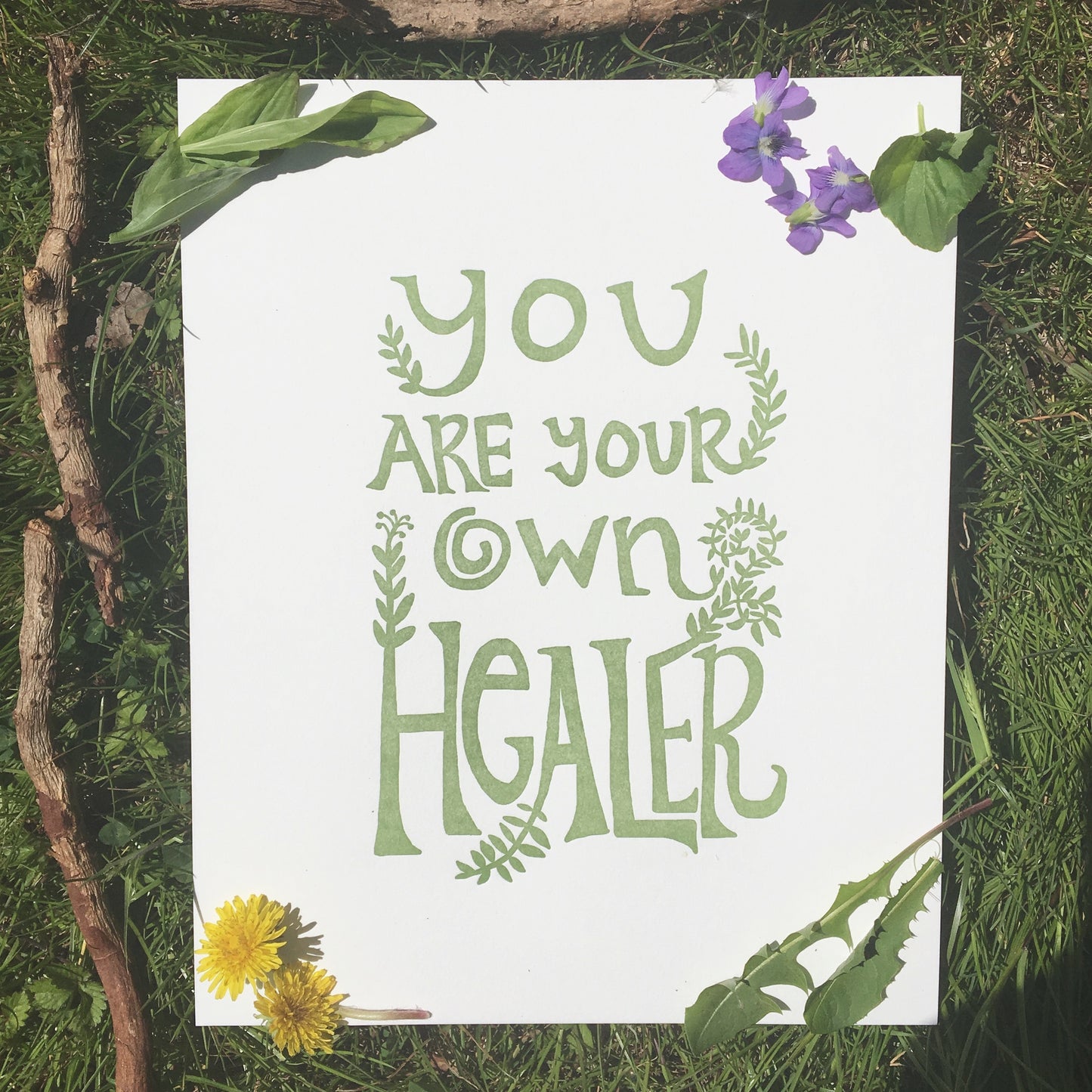 High quality Letterpress Art Print featuring original hand-drawn typography by Macon York that reads "you are your own hearler" in a funky, earthy, 70s style. 8" x 10" Easily fits into a standard frame. Print is shown outdoors on the grass on a sunny day. Local herbs are placed around the print: dandelion, violet, plantain, and sassafrass bark.