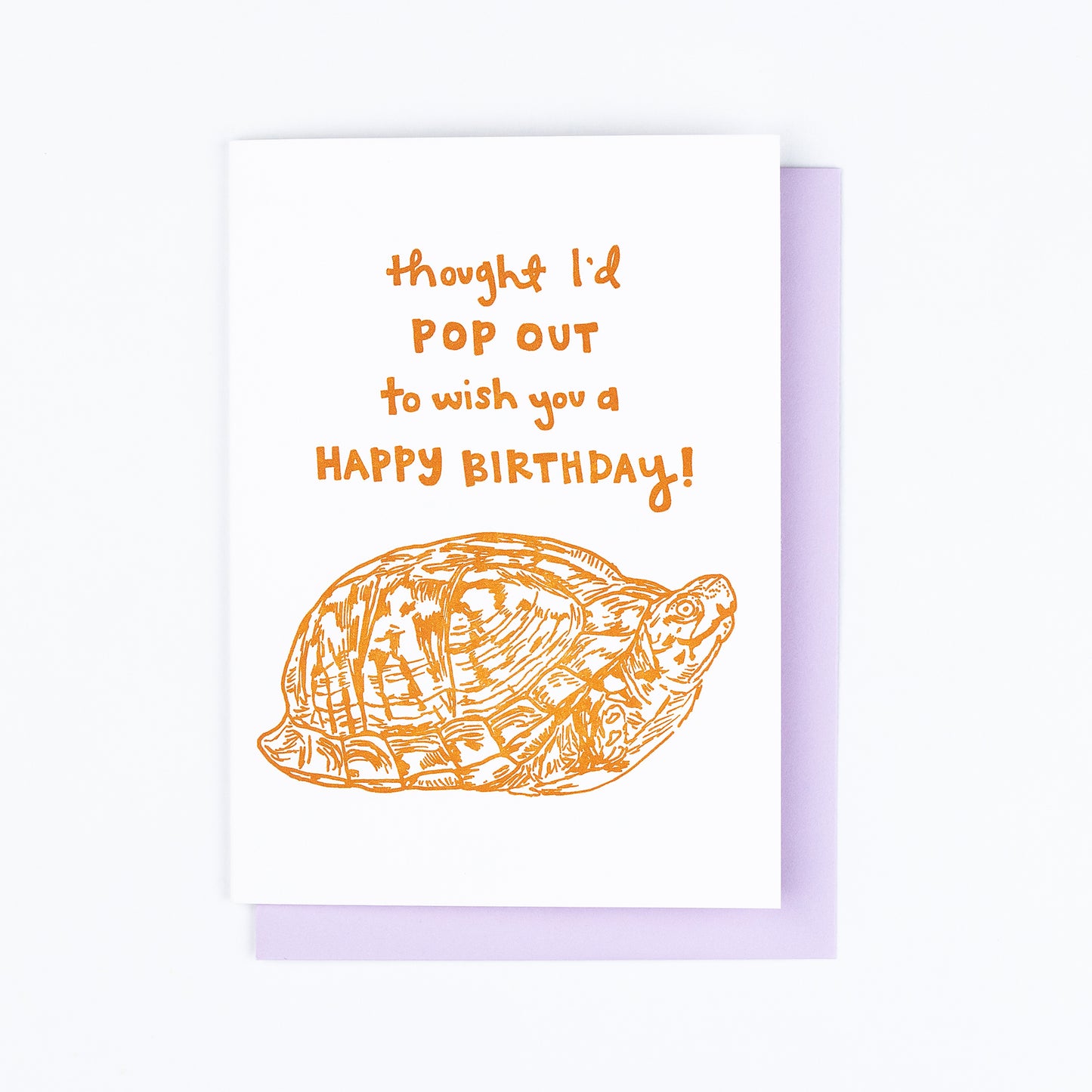 Letterpress greeting card featuring a hand-drawn Appalachian Box Turtle printed in a vibrant dark orange ink. "Thought I'd pop out to wish you a Happy Birthday!" is written on the top of the card in a whimsical hand-drawn text, in the same orange ink. The card is white, blank inside, and is paired with a lilac purple envelope.