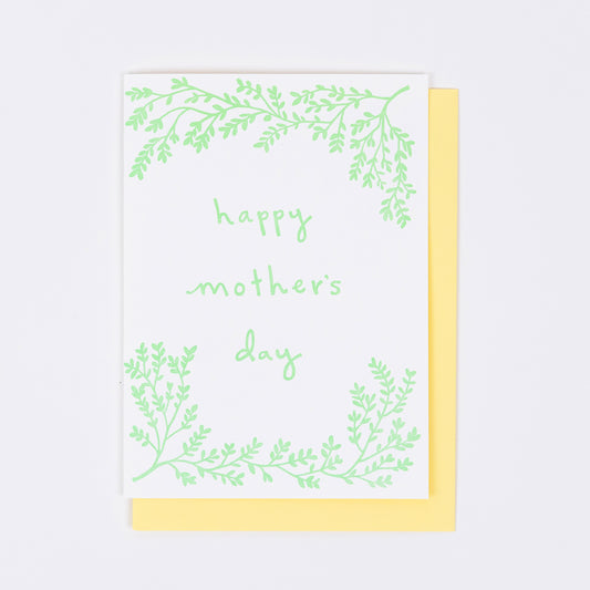 Letterpress greeting card featuring hand-drawn branches, printed in a soft minty green ink. The center of the card says "Happy Mother's Day" in a whimsical hand-drawn text, in the same minty green ink. The card is white, blank inside, and is paired with a warm yellow envelope.