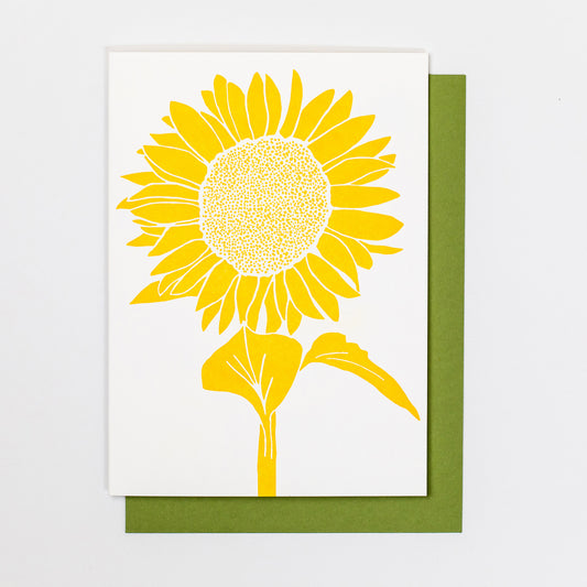 Letterpress greeting card featuring a cheeful Sunflower, printed in a vibrant golden-yellow ink. There is no text on the card. The white card is 100% cotton, blank inside, and is paired with a rich green envelope.