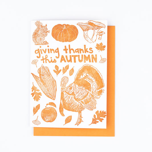 This cheerful Autumn card features all the iconic images of the fall season: squirrel, heritage pumpkin, mushrooms, fall leaves (maple, oak, sassafras, and ginkgo), a tom turkey, corn harvest, and a fresh-picked apple. Perfect for Thanksgiving. Vibrant orange ink paired with an orange envelope. Blank interior.