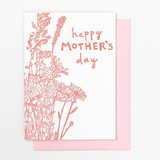 Letterpress greeting card featuring a hand-drawn wildflower bouquet, printed in a vibrant pink ink. The top center of the card says "Happy Mother's Day" in a whimsical hand-drawn text, in the same pink ink. The card is white, blank inside, and is paired with a light pink envelope.
