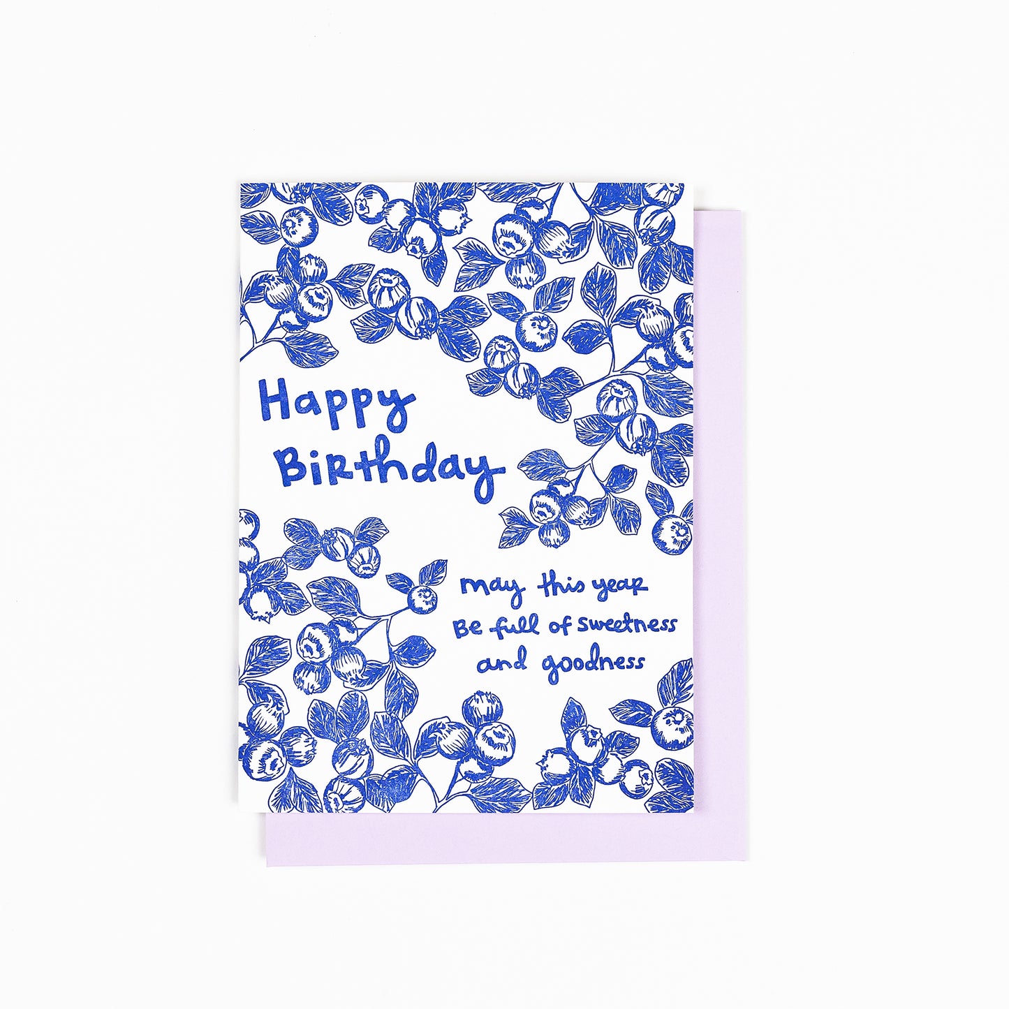 Letterpress greeting card featuring hand-drawn blueberries printed in an vibrant blue ink. "Happy Birthday! May this year be full of sweetness and goodness" is written on the card in a whimsical hand-drawn text, in the same blue ink. The card is white, blank inside, and is paired with a soft lilac envelope.