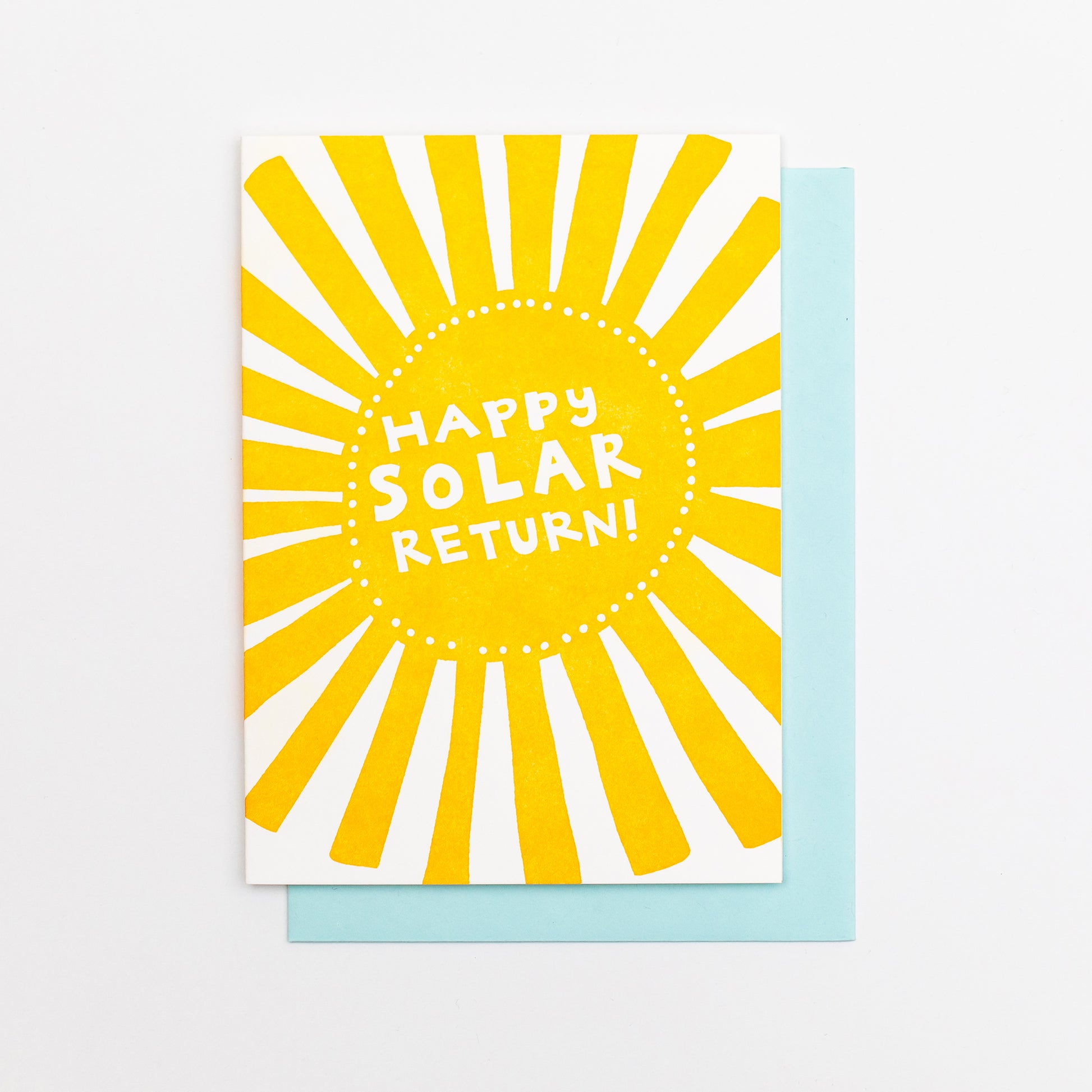 Letterpress greeting card featuring a hand-drawn Sun printed in a vibrant orange-gold ink. "Happy Solar return!" is written in the center of the sun in a whimsical hand-drawn text, in a knockout white. The card is white, blank inside, and is paired with a light sky blue envelope.