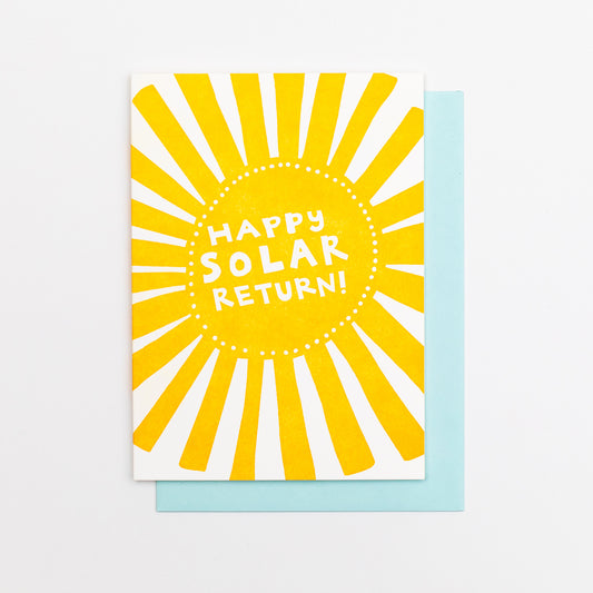 Letterpress greeting card featuring a hand-drawn Sun printed in a vibrant orange-gold ink. "Happy Solar return!" is written in the center of the sun in a whimsical hand-drawn text, in a knockout white. The card is white, blank inside, and is paired with a light sky blue envelope.