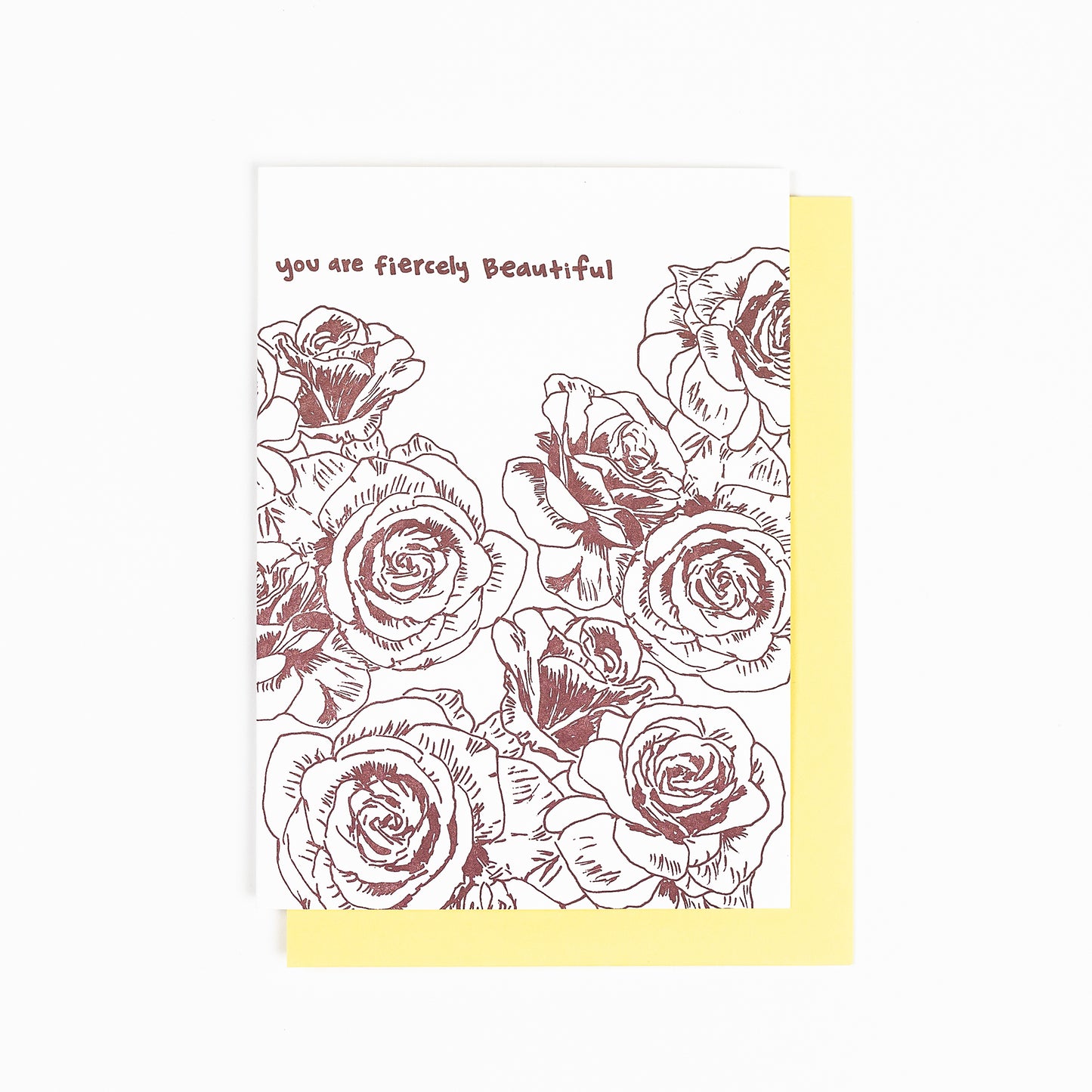 Letterpress greeting card featuring hand-drawn rose flowers printed in a rich, warm brown ink. Whimsical hand-drawn text saying "you are fiercely beautiful" is shown at the top of the card, in the same brown ink. The card is white, blank inside, and is paired with a soft yellow envelope.