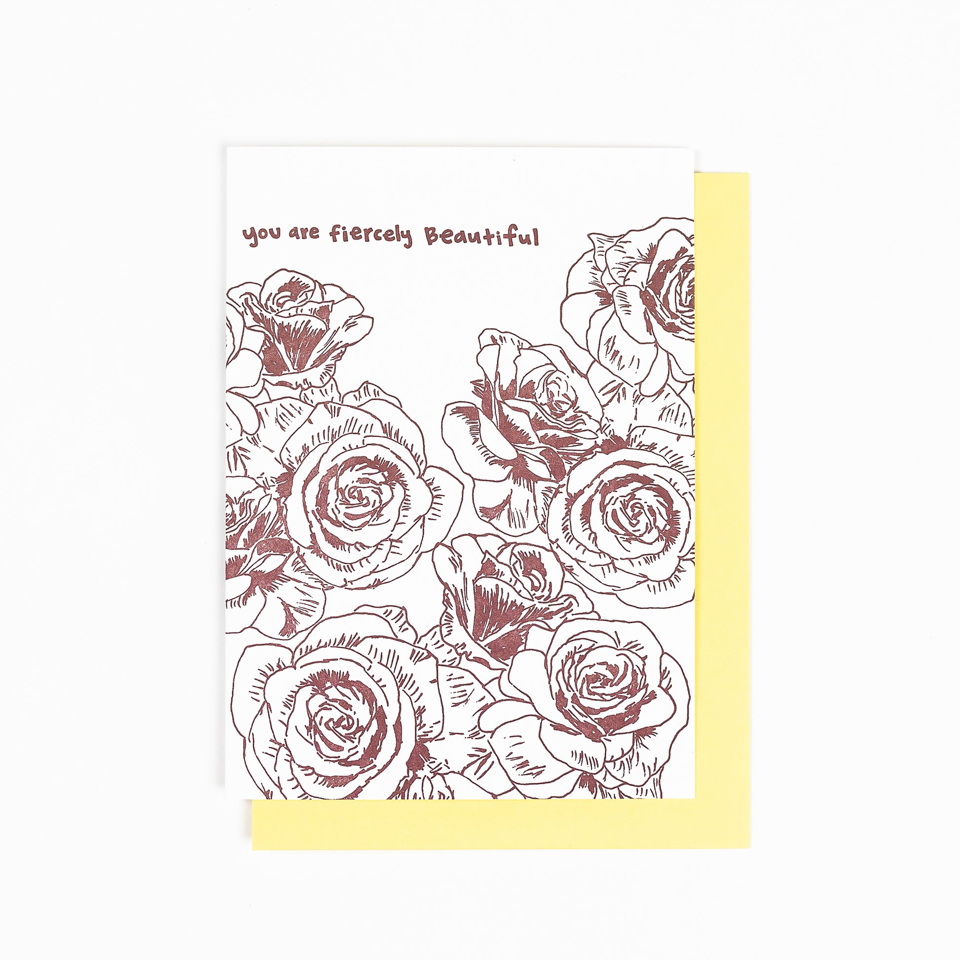 Letterpress greeting card featuring hand-drawn rose flowers printed in a rich, warm brown ink. Whimsical hand-drawn text saying "you are fiercely beautiful" is shown at the top of the card, in the same brown ink. The card is white, blank inside, and is paired with a soft yellow envelope.