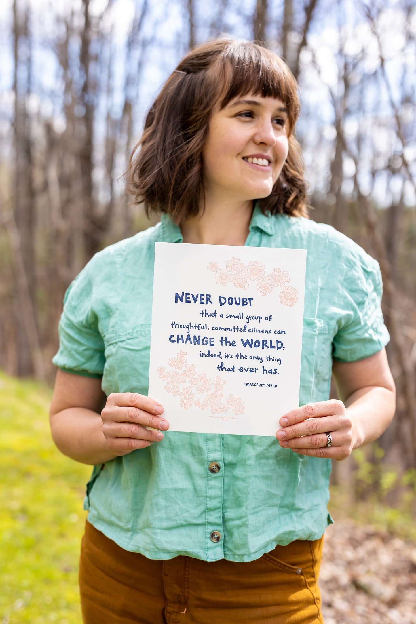 This letterpress print features original text by Margaret Mead, hand-drawn in a funky folk-art style of Macon York: "Never doubt that a small group of thoughtful, committed citizens can change the world, indeed, it's the only thing that ever has." Hand-drawn coreopsis and phlox in cheerful coral ink and hand-lettered text in navy. The artist, Macon, is holding the print outside in the sunshine on an early Spring day.