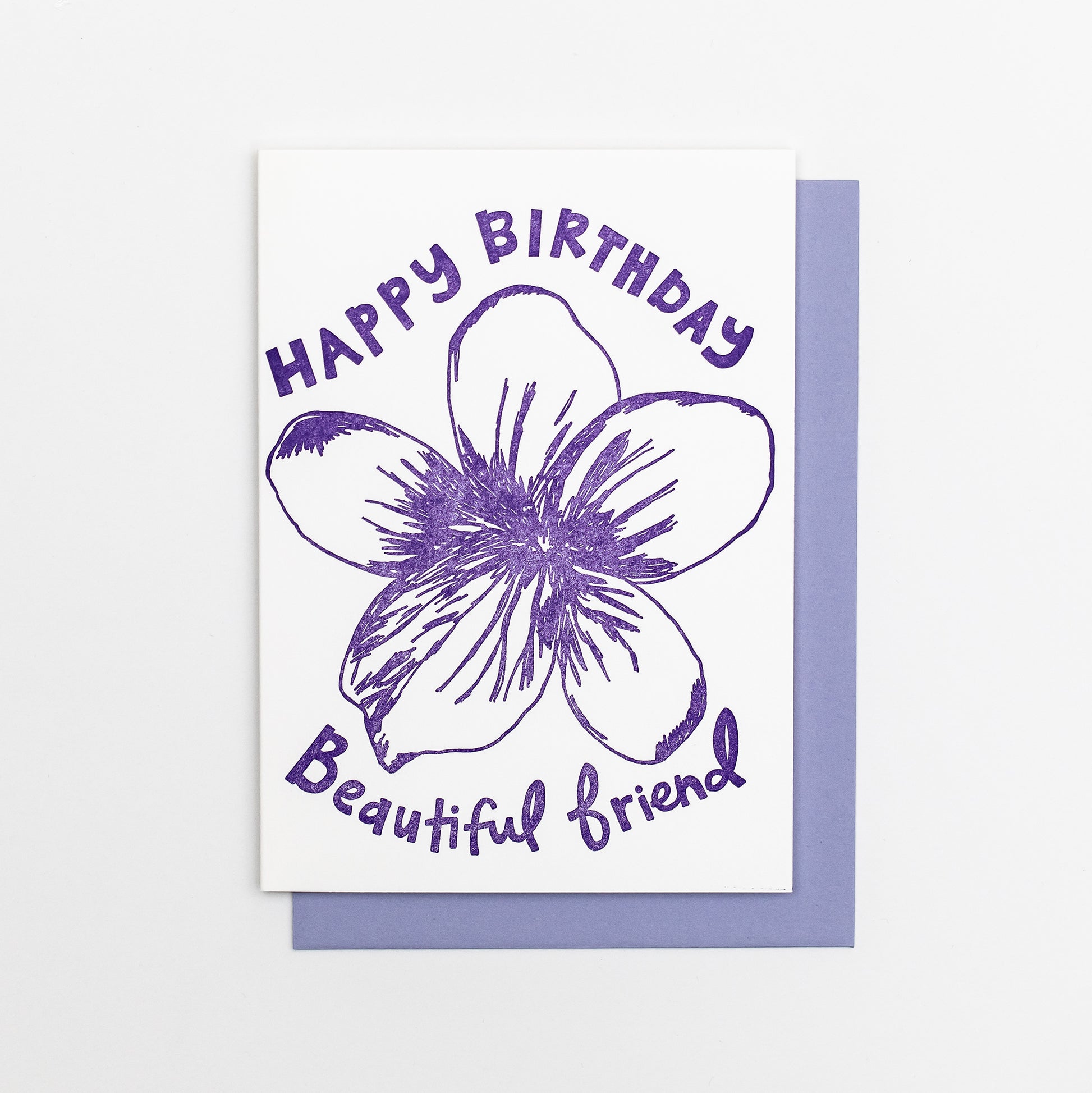Letterpress greeting card featuring a hand-drawn Violet flower printed in a vibrant purple ink. "Happy Birthday Beautiful Friend!" is written on the top and bottom of the flower in a whimsical hand-drawn text, in the same purple ink. The card is white, blank inside, and is paired with a lilac purple envelope.