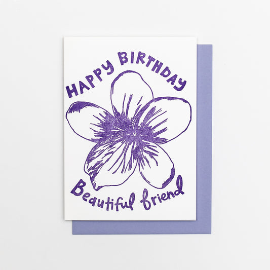 Letterpress greeting card featuring a hand-drawn Violet flower printed in a vibrant purple ink. "Happy Birthday Beautiful Friend!" is written on the top and bottom of the flower in a whimsical hand-drawn text, in the same purple ink. The card is white, blank inside, and is paired with a lilac purple envelope.
