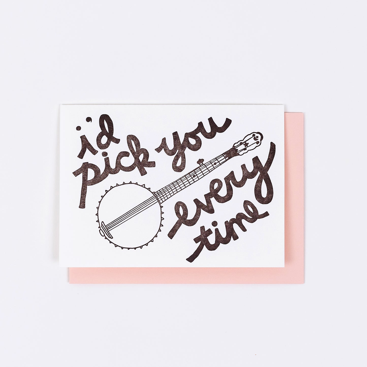 Letterpress greeting card featuring a hand-drawn banjo, printed in an earthy brown ink. Whimsical hand-drawn text saying "I'd Pick You Everytime" surrounds the banjo, in the same pink ink. The card is white, blank inside, and is paired with a light pink envelope.