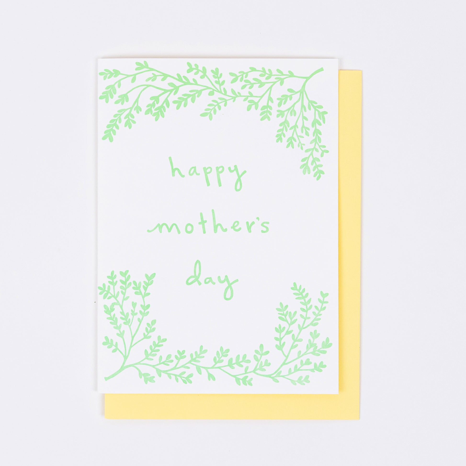 Letterpress greeting card featuring hand-drawn branches, printed in a soft minty green ink. The center of the card says "Happy Mother's Day" in a whimsical hand-drawn text, in the same minty green ink. The card is white, blank inside, and is paired with a warm yellow envelope.