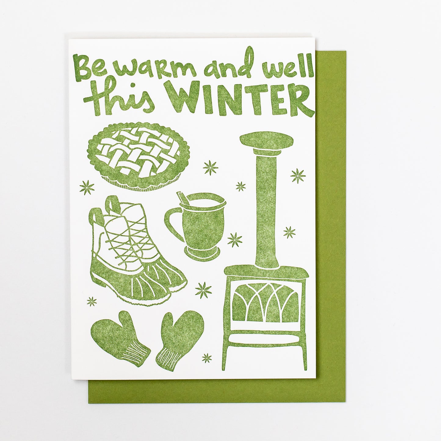 Celebrate Winter with this festive greeting card! This cheerful and cozy card features all the iconic image of the winter season: wood burning stove, star anise, hot cocoa (or cider!), fresh baked pie, mittens, winter boots. Hand-drawn images and typography are letterpress-printed in forest green ink. Green envelope. 