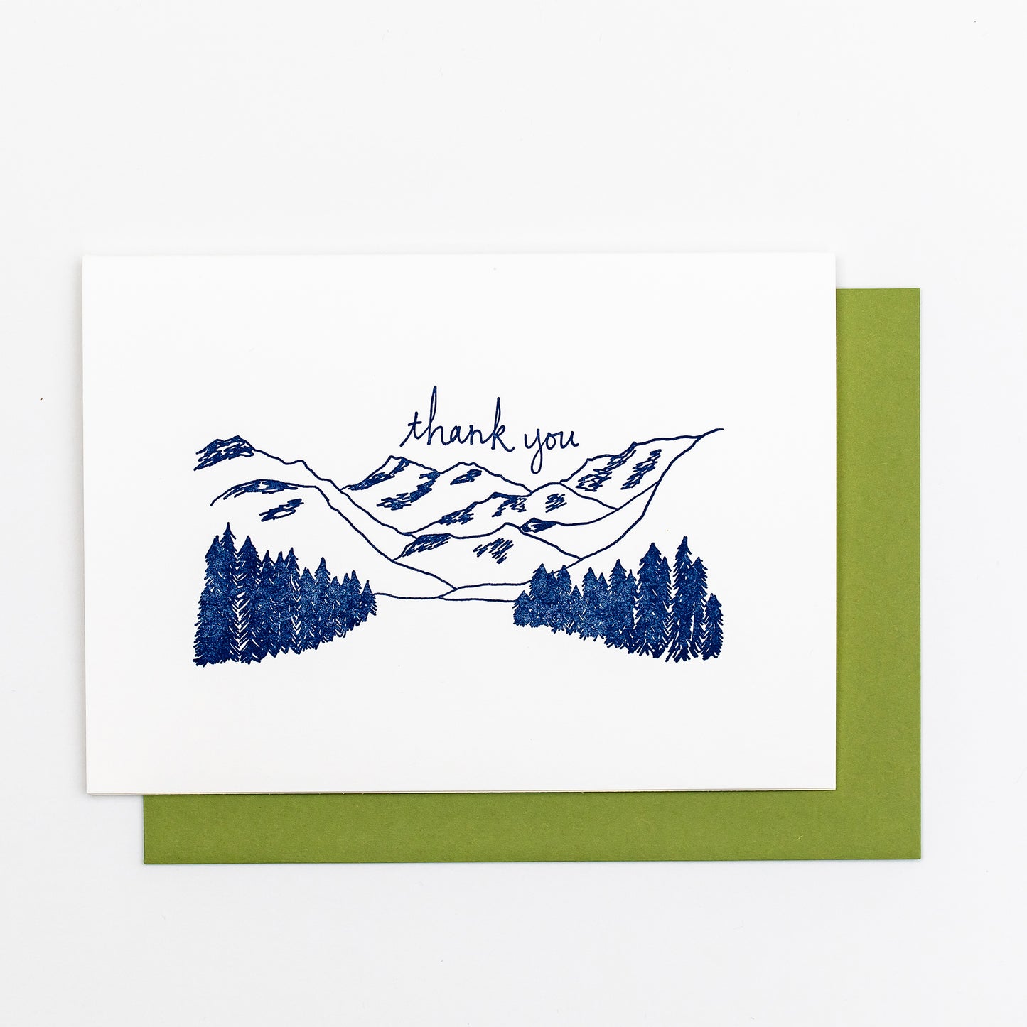 Letterpress greeting card featuring hand-drawn mountain landcape, printed in a rich navy ink. Whimsical hand-drawn text saying "Thank you" is shown above the moutains, in the same navy ink. The card is white, blank inside, and is paired with a rich green envelope.